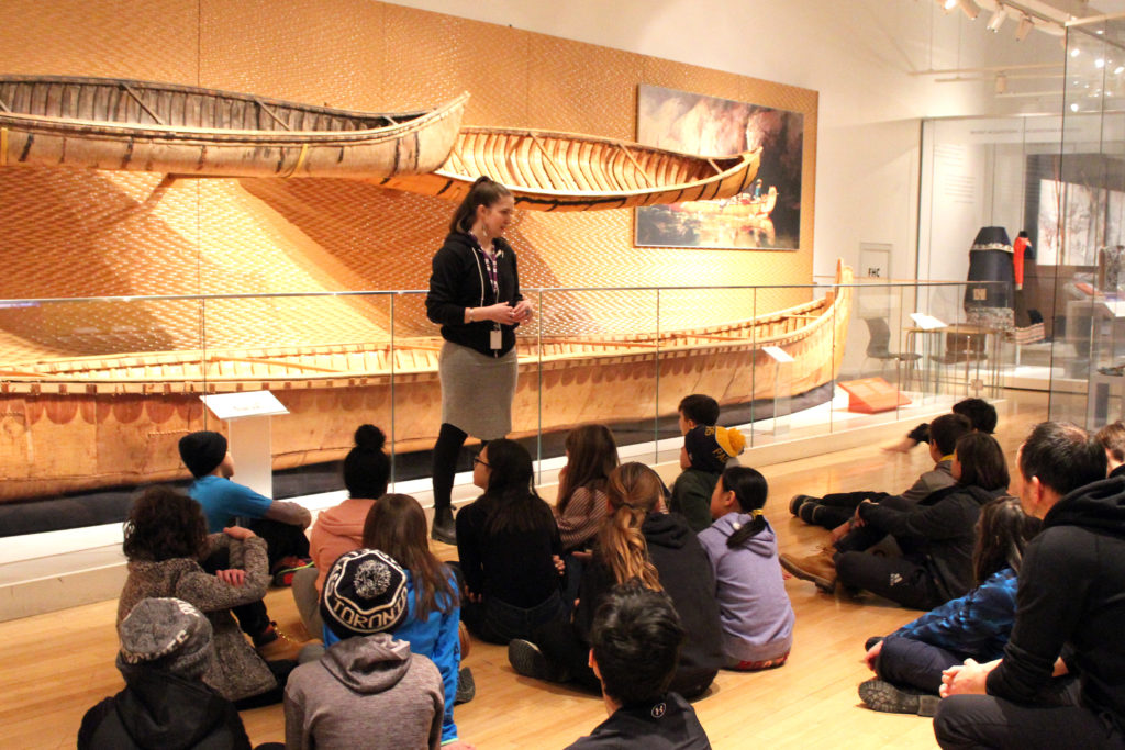 Royal Ontario Museum's Hack the ROM program. Indigenous student group with presenter in front of birchbark canoes